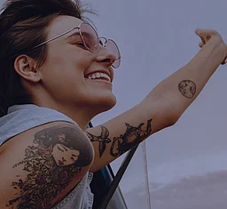 Tättowierte Frau hebt strahlend ihren Arm in den Wind